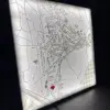 Straßenkarte in 3D rund um eine Wunschadresse. Die Adresse wird mit einem roten Herz markiert. Die Karte sitzt in einem Rahmen, der beleuchtet werden kann.
